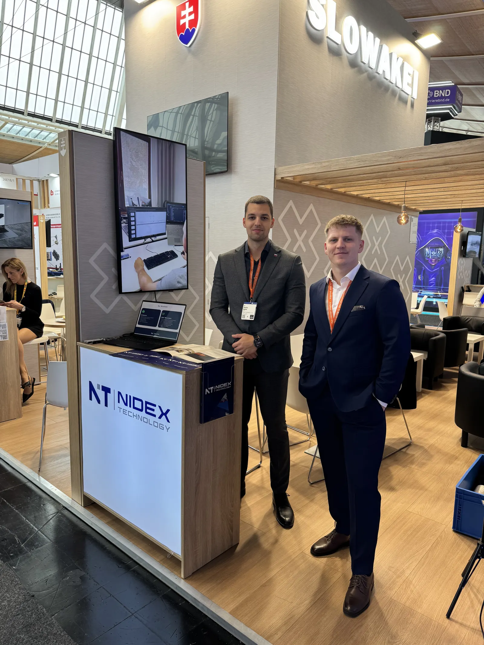 Zakladatelia Nidex Technology v oblekoch pri stánku NIDEX na veľtrhu